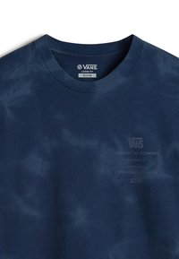 Mörkblå t-shirt i bomull, med en lös passform och ett subtilt tie-dye-mönster, samt tryckt text som beskriver varumärke och ursprung.