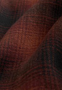 Texturiertes Gewebe mit einem rot-schwarzen Karomuster. Das Material wirkt weich mit einer warmen, strukturierten Oberfläche.