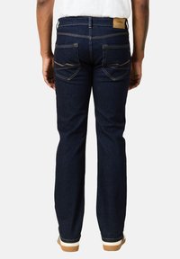 Jeans in denim blu scuro con taglio dritto, caratterizzati da cuciture a contrasto, due tasche posteriori e un'etichetta in pelle sul cinturino.