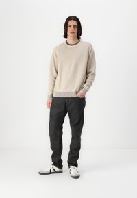Suéter de punto acanalado beige con un cuello oscuro, combinado con pantalones cargo oscuros tapered con bolsillos, llevados con zapatillas blancas.