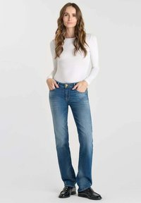 Jean en denim bleu avec un design à jambe droite, lavage plus clair et couture contrastée, associé à un haut à manches longues blanc.