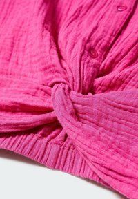 Haut rose vif avec un design noué à la taille, tissu texturé et détails de boutons sur le devant. Matière légère et respirante.