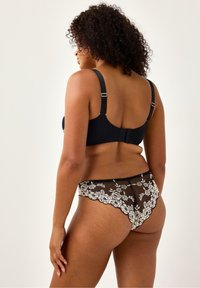 Sort blonde BH med justerbare stropper, der har blomsterbroderi. Sort mesh-tanga med blomster-lacet trim og bølgede kanter.