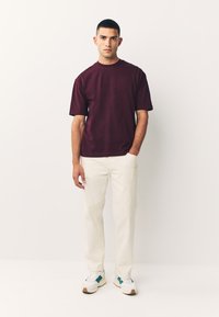 Bordeauxrode katoenen T-shirt met korte mouwen, gecombineerd met off-white broek en witte sneakers met teal accenten. Eenvoudige, ontspannen pasvorm.