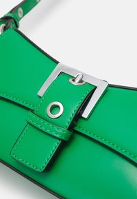 Vihreä tekonahkainen käsilaukku, jossa on hopeinen solkilukko. Laukussa on litteä muotoilu ja mustat ompeleet kontrastina reunoilla.