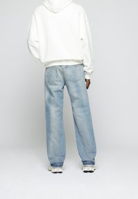 Jeans bleu clair ample avec un lavage délavé, associés à un sweat à capuche blanc. Caractéristiques : jambes droites et poches arrière standards.