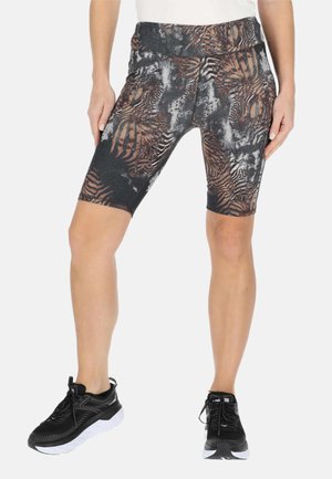 Benen met zwarte en bruine abstracte patroon knielange sportshorts en zwarte hardloopschoenen met witte zolen.
