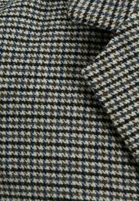 Svart, vitt och grått houndstooth-tyg med subtila blå rutor, som visar struktur och en vikt del.