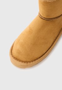Botte d'hiver en daim beige avec un bout arrondi et une semelle cousue sur un fond blanc uni.
