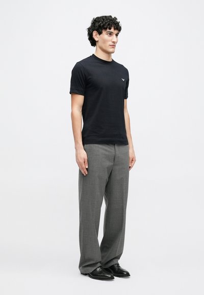 Juoda trumpomis rankovėmis marškinėliai su apvalia iškirpte, derinami su pilkomis tiesaus kirpimo kelnėmis. Audinys atrodo lygus, o siluetas prigludęs.