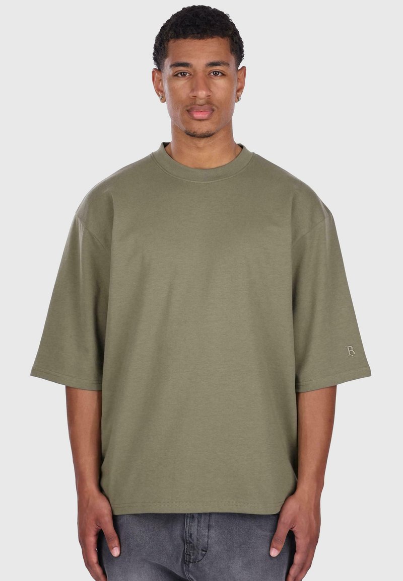 T-shirt oversize a maniche corte color verde oliva realizzato in cotone; presenta un colletto rotondo e un piccolo logo sulla manica sinistra.