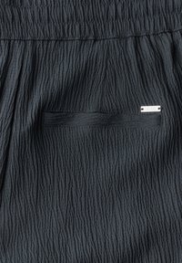 Shorts en tissu texturé noir avec un motif en ondulation subtil, taille élastique et une petite poche cousue avec un accent de logo métallique.