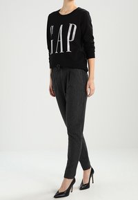 Felpa nera con logo "GAP" argentato, abbinata a pantaloni grigi a righe e tacchi alti neri. Tessuto morbido e vestibilità sartoriale.