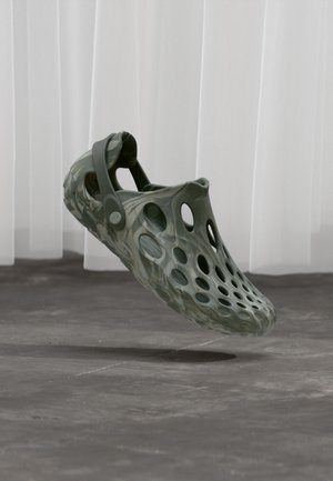 Green marbled clogs featuring a hollow design, side strap, and large circular vents for breathability. Made from lightweight, flexible material.