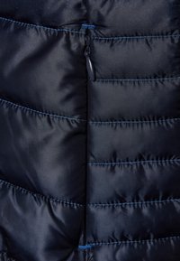 Polstret marineblå jakke med kviltet design, udstyret med sort lynlås og kontrastfarvet blå syninger. Glat tekstur, letvægtsstof.