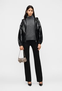 Γυναίκα που φορά μαύρο δερμάτινο μπουφάν, γκρι πουλόβερ με ζιβάγκο, μαύρο παντελόνι, μαύρες ψηλοτάκουνες γόβες και κρατά μια μικρή καφέ τσάντα χειρός.