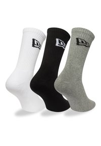 Trois paires de chaussettes de crew : blanches, noires et grises. Chacune possède une texture côtelée et un petit logo noir brodé sur le bord.