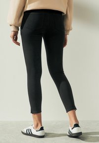 Zwarte skinny jeans van rekbaar materiaal, met een hoge taille, subtiele vervaging en raw hems. Gepaard met witte sneakers.