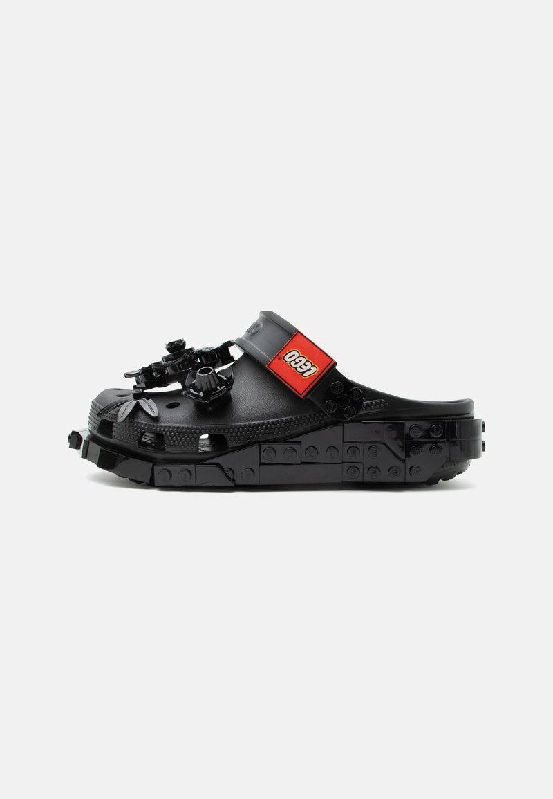 Μαύρο clog στυλ Crocs με σόλα από τουβλάκια LEGO και διακοσμήσεις LEGO στην κορυφή, με κόκκινο λουράκι με το λογότυπο LEGO.