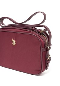 Borsa a tracolla color bordeaux con una texture liscia, dettagli dorati e logo visibile. Presenta una tracolla regolabile e una chiusura con zip.