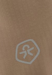 Abstraktus pilkas logotipas arba emblema ant tekstūrinio rudo audinio su zigzaginio rašto motyvu.