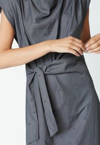 Rochie gri cu decolteu drapat și mâneci scurte, dotată cu un cordon la talie și o textură subtilă cu mici modele verticale.