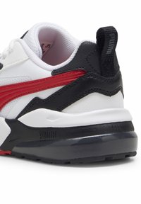 Sneaker bianca e nera con dettagli rossi, dotata di una tomaia testurizzata, colletto imbottito e una robusta suola in gomma nera con dettagli del logo.