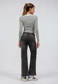 Black and white striped long-sleeve top, fitted at the waist, paired with high-waisted, gray flared jeans, and white sneakers with black accents.