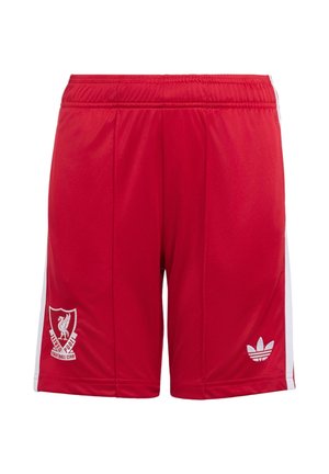 To børn iført hvide og røde Liverpool-fodbolddragter, den ene holder en sort-hvid fodbold, stående på en ensfarvet baggrund.