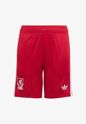 To børn iført hvide og røde Liverpool-fodbolddragter, den ene holder en sort-hvid fodbold, stående på en ensfarvet baggrund.