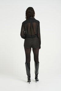 Musta läpinäkyvä pitkähiha blouse, kuvioidut korkeavyötäröiset shortsit ja kiiltävät mustat polvipituiset saappaat, esitetty takaa.