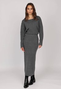 Robe longue ajustée en tissu tricoté texturé gris, avec des manches longues et un col rond, assortie à des bottines noires. 