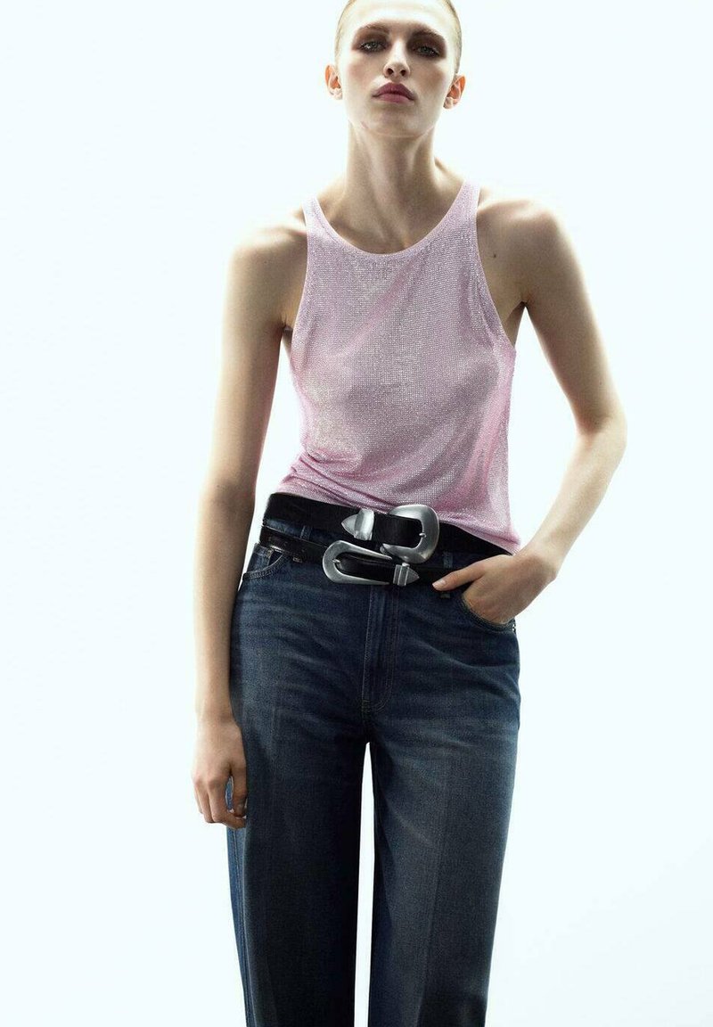 Top sin mangas de metalizado rosa combinado con jeans de tiro alto en azul oscuro. Cinturón negro con gran hebilla plateada como acento. Textura suave en general.