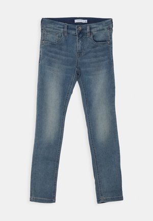 Blå falmede denim skinny jeans med forlommer, bæltestropper og knaplukning, lagt fladt på en hvid baggrund.