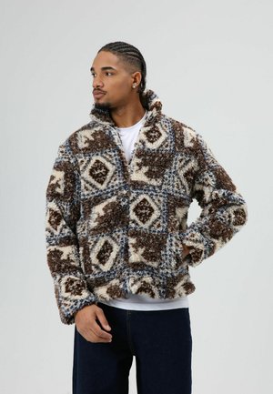 Wollen, meerkleurig jack in bruin, crème en blauw met een geometrisch patroon, hoge kraag en brede mouwen. Zachte textuur en losse pasvorm.