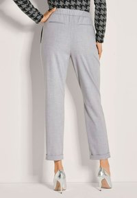 Vrouw in grijze tapering broeken met opgerolde hems, gecombineerd met zilveren hoge hakken en een zwart-grijze houndstooth top.