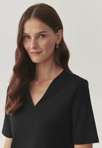 Haut noir à manches courtes en tissu lisse, doté d'un décolleté en V, de lignes épurées et de détails de couture subtils.