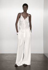 Witte, loszittende broek en een bijpassende, gerimpelde mouwloze top met een v-hals. De stof lijkt lichtgewicht en textuur te hebben.