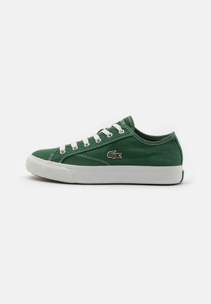 Zapatillas de lona verdes con cordones blancos, suelas de goma y un pequeño logotipo bordado en el lateral. Diseño de punta redondeada y bajo perfil.