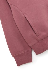 Detalle de sudadera burdeos con puños acanalados, textura suave y bolsillo lateral. La tela es suave con un ligero estiramiento.