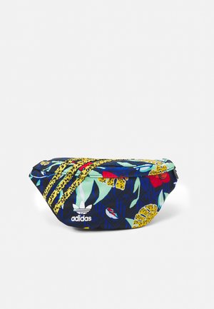 Sac banane Adidas avec imprimé floral tropical et motif léopard, comportant trois accents rayés jaunes et logo Adidas blanc sur fond bleu foncé.
