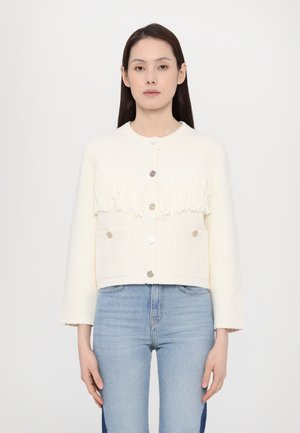 White cropped cardigan with fringe detail, large silver buttons, and two front pockets. Features ribbed texture along the edges and sleeves.