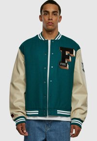 Jachetă de tip varsity în nuanțe de teal și crem, cu un logo brodat „F” și manșete cu dungi. Dispune de nasturi tip snap și o croială lejeră.