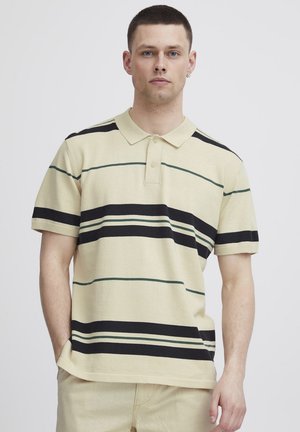 Camisa polo crema con rayas horizontales negras y verdes, de manga corta y con una tapeta de tres botones, hecha de un tejido suave y texturizado.