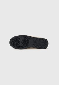 Suola di sneaker in gomma nera con battistrada testurizzato, motivi circolari e angolari, con un accento beige vicino al lato per stabilità.