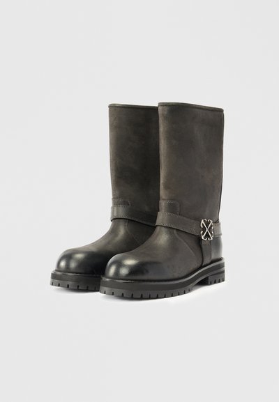 Botas altas de camurça pretas com bico arredondado, parte superior texturizada e um detalhe decorativo em fivela prateada de tom prateado na lateral. Sola de borracha.