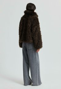 Brun, lurvig pälsjacka med hög krage, i kombination med löst sittande grå denimjeans. Texturen på jackan är framträdande.