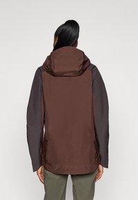 Giacca da esterno marrone e grigio scuro con cappuccio, caratterizzata da un tessuto morbido, un design strutturato e polsini regolabili.