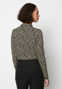Maglia a maniche lunghe con un motivo astratto bianco e nero, caratterizzata da un colletto alto. Abbinata a pantaloni neri, che evidenziano una silhouette aderente.