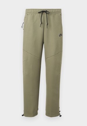 Ελιά πρασινωπό παντελόνι φόρμας Nike με μαύρα κορδόνια, φερμουάρ στην πλαϊνή τσέπη, ένθετα στα γόνατα και ρυθμιζόμενους δεσμούς στον αστράγαλο.